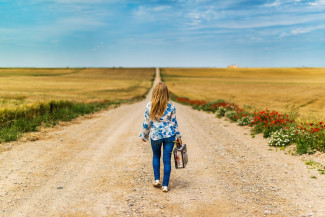 Frau von hinten auf Feldweg mit Koffer in der Hand