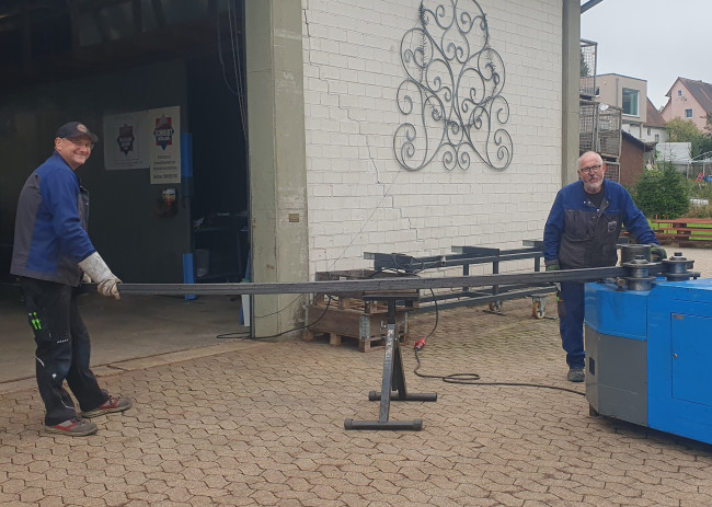 Zwei Männer biegen ein langes Stück Stahl